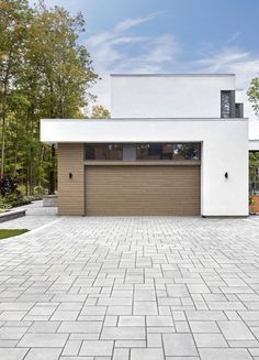 a white house with a brown garage door and brick driveway in front of the house