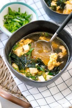 two bowls filled with tofu and spinach on top of a white table cloth