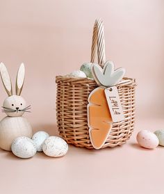 an easter basket with eggs and bunny ears next to it, on a pink background