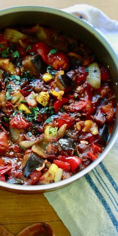 a pot filled with lots of vegetables on top of a wooden table next to a spoon