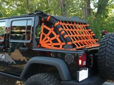 a jeep with an orange cage on the back is parked in front of some trees