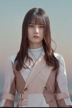 a woman with long brown hair wearing a white shirt and beige skirt standing in front of the ocean