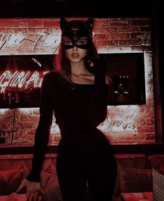 a woman wearing a cat mask standing in front of a brick wall with neon signs