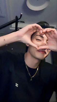 a person making a heart with their hands in front of the camera while wearing a black shirt