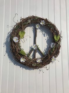 a peace sign made out of twigs and flowers on a white wall with green leaves