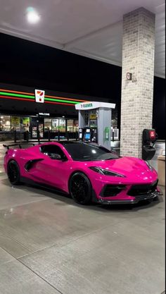 a pink sports car is parked in front of a gas station with no one around