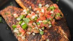 two fish fillets with tomatoes and green onions on top in a black skillet