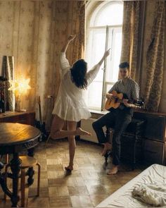 a man and woman are playing guitar in a room with a large window, while another plays the guitar