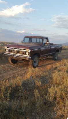 an old pick up truck parked on the side of a dirt road near dry grass