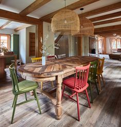 a wooden table surrounded by colorful chairs in a room with exposed beams and wood flooring