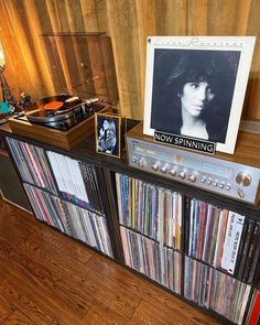 an old record player is on top of a shelf full of records and cds in front of a poster