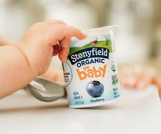 a baby is holding a spoon in front of a yogurt container