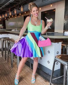 a woman in a multicolored dress is holding a drink and posing for the camera