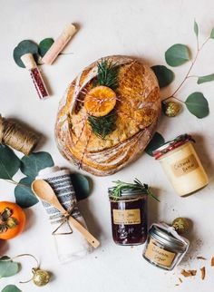 bread, jams and other items are arranged on a white surface with greenery