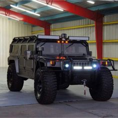 an armored vehicle with lights on is parked in front of a warehouse door and yellow beams