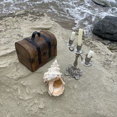 a wooden box sitting on top of a sandy beach next to a candle holder and seashell