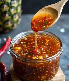 a spoon full of chili sauce being drizzled over the top of a jar