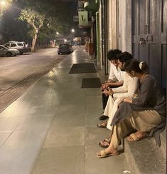 two people sitting on the curb looking at their cell phones