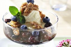 a glass bowl filled with ice cream and blueberries on top of a table next to flowers