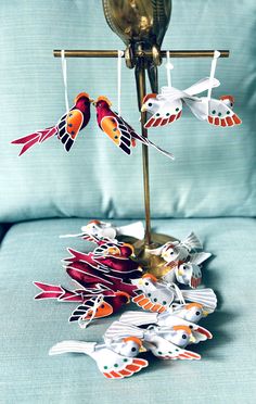 several colorful birds are hanging from a hook on a lamp stand in front of a blue couch