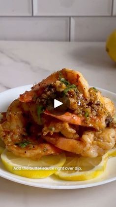 a white plate topped with shrimp and lemon wedges on top of a marble counter