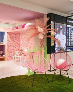 two pink chairs sitting on top of a lush green floor next to a wall covered in pictures