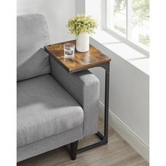 a gray couch with a wooden end table on it and flowers in a white vase