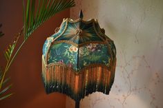 a green lamp with fringes on it next to a palm tree and wallpaper