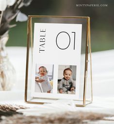 a table number frame with two pictures of babies on it and a vase full of flowers in the background