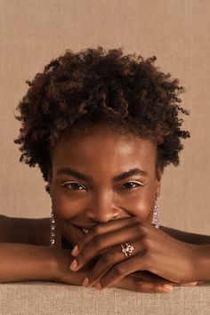 a woman with short hair smiling at the camera and wearing earrings on her head, in front of a beige background