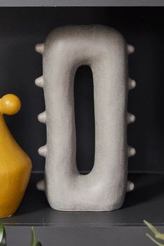 a yellow vase sitting on top of a shelf next to an o shaped like a bird