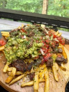 a wooden plate topped with french fries covered in guacamole and toppings