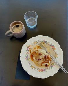 a plate with some food on it next to a cup of coffee and a spoon