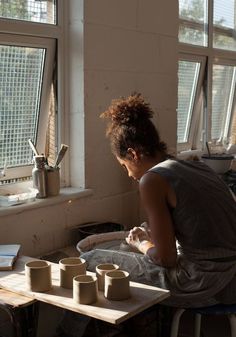 a woman sitting at a table with four cups on it and looking out the window