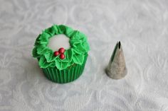 a cupcake decorated with green icing next to a small silver object on a white tablecloth