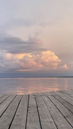 an empty wooden dock with water and clouds in the background