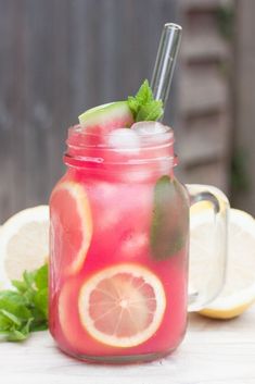 a mason jar filled with watermelon lemonade and mint garnish next to sliced lemons