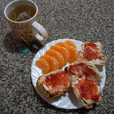 an open face sandwich with jam and orange slices on a plate next to a cup of tea