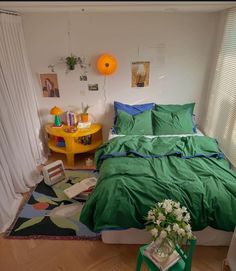 a bed with green sheets and pillows in a bedroom next to a yellow side table