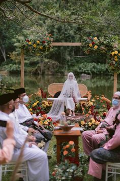 a group of people sitting around a wooden table with flowers on it and one person wearing a white veil