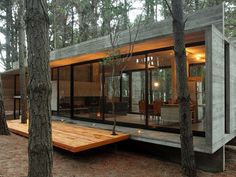 a small cabin in the woods with wood flooring and glass walls, surrounded by trees