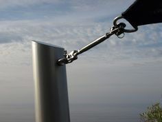 a metal pole with a chain hanging off it's side near the ocean under a cloudy blue sky