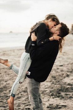 a man and woman kissing on the beach while holding each other in front of them