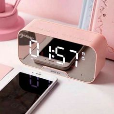 an alarm clock and cell phone sitting on a table next to a pink telephone charger