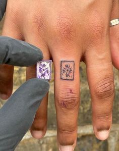 a person's left hand with a small tattoo on the middle finger and purple flowers