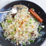 a black plate topped with rice, carrots and celery next to a spoon