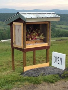 a chicken coop with an open sign in the grass next to it on top of a hill