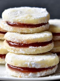 a stack of jelly filled cookies sitting on top of a white plate with powdered sugar