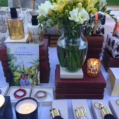 a table topped with lots of books and vases filled with flowers next to candles