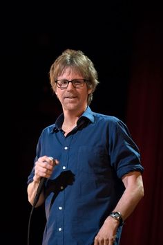 a man standing in front of a microphone with his hand on the mic and wearing glasses